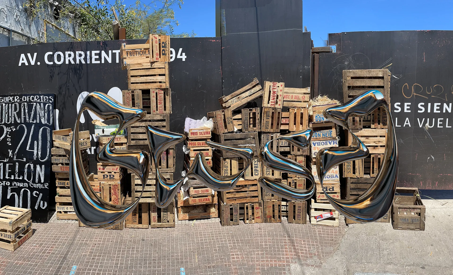 Escultura cromada 3D de formas curvas frente a una pila de cajones de fruta en la avenida Corrientes