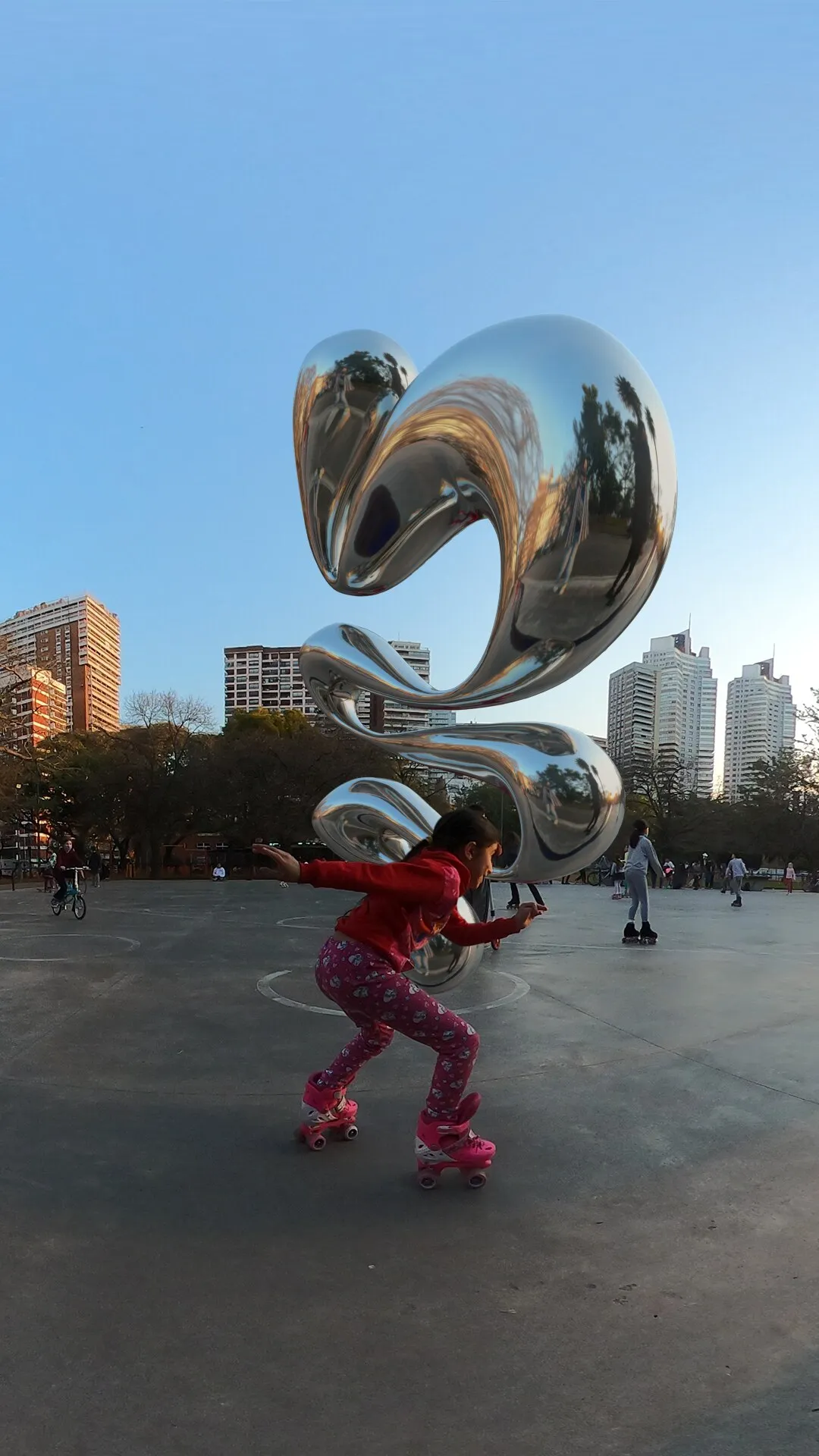 Escultura cromada 3D flotando sobre una plaza con patinadores