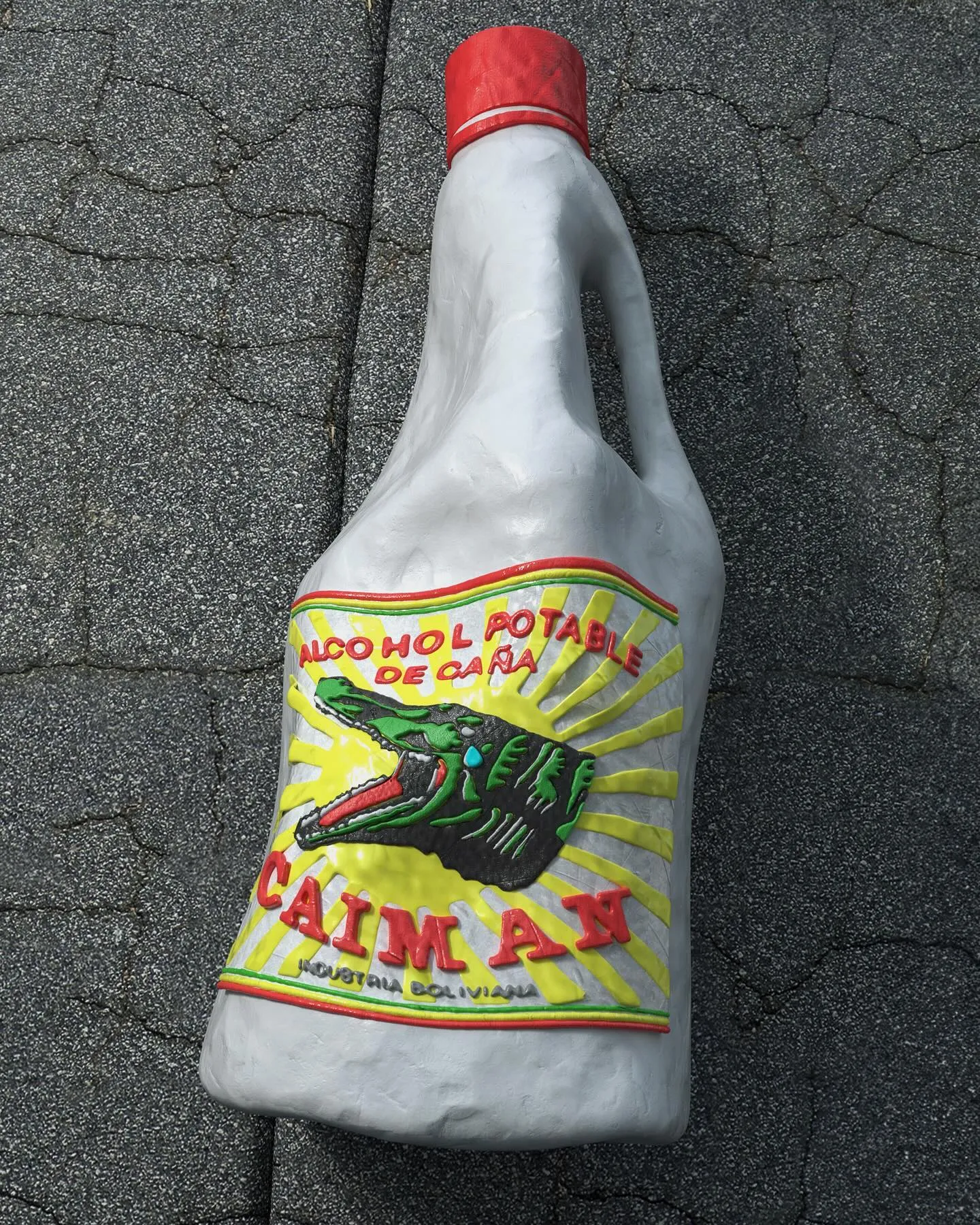 Escultura 3D de plastilina: una botella blanca de alcohol potable Caimán apoyada sobre asfalto
